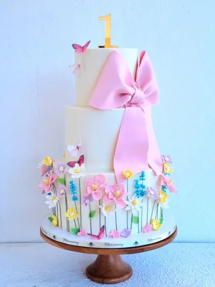 A classic three-tiered cake perfect for a first birthday, featuring a large, structured fondant bow and a garden of delicate sugar flowers. I teach how to create bows that hold their shape and arrange flowers for a beautiful, balanced design.