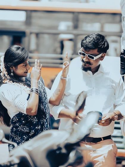 A fun, retro-style shot of a couple trying on sunglasses from a street vendor, with a classic yellow bus in the background.