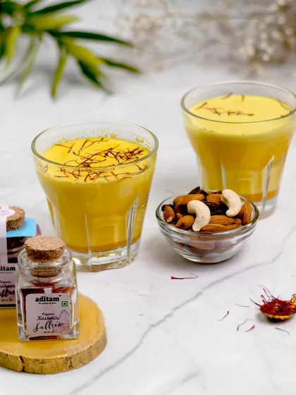 Two glasses of golden turmeric milk (haldi doodh) are garnished with saffron and styled with nuts and saffron jars. This cozy and inviting shot highlights a healthy, traditional Indian beverage.