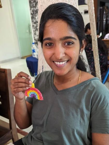 A smiling student holding her colorful rainbow keychain, a fun and quick project.