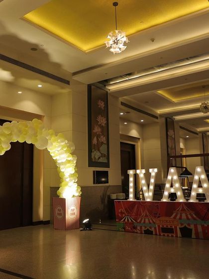 The entrance area for a carnival party, featuring a balloon arch and large, illuminated marquee letters spelling the birthday boy's name.