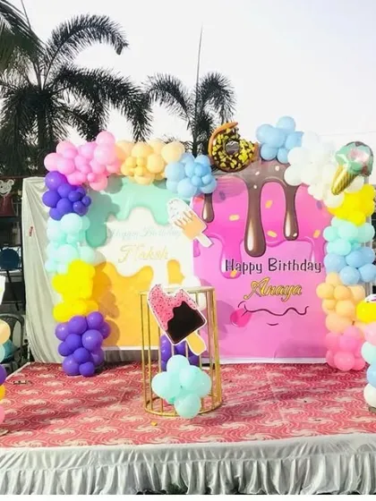 A sweet ice cream themed birthday party. This outdoor stage setup includes a "Happy Birthday" backdrop, ice cream cone props, and a colorful balloon arch.