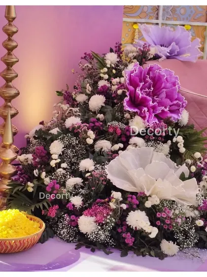 A lush floral arrangement with large purple and white paper flowers, designed to flank the main seating at a Mehendi party.