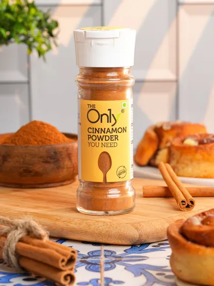 A bottle of cinnamon powder styled in a kitchen setting with fresh cinnamon rolls. This lifestyle approach helps customers imagine using the product in their own cooking.