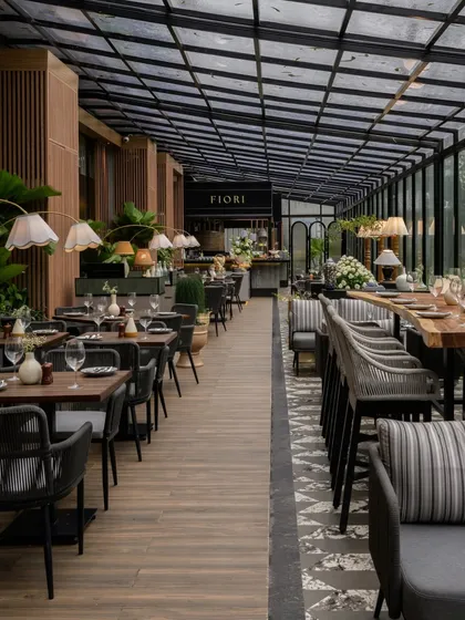 The al fresco dining area at FIORI, Lonavala, where the design seamlessly merges with the surrounding nature. A retractable glass roof and full-height windows allow for an immersive experience, complemented by a natural material palette of stone and wood-finished aluminum.