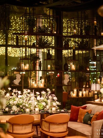 A candlelit seating area at the glass house reception, with a backdrop of industrial-style shelves filled with plants and candles. The design layered textures and lighting to create depth and intimacy.