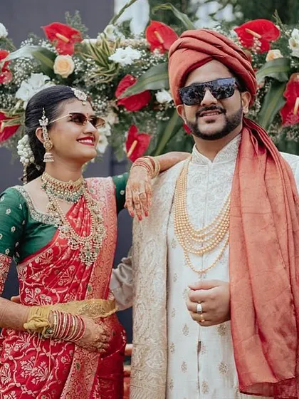 A cool couple shot with the bride in a red and green saree. Her custom green blouse features intricate embroidery, adding a touch of glamour to her wedding look.