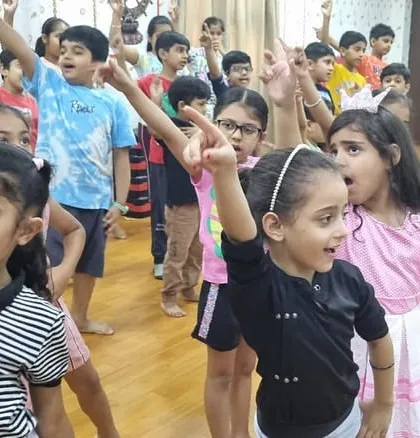 Children enthusiastically follow along with an instructor during a dance routine. Their raised arms and engaged expressions show how we make learning new skills an exciting experience.