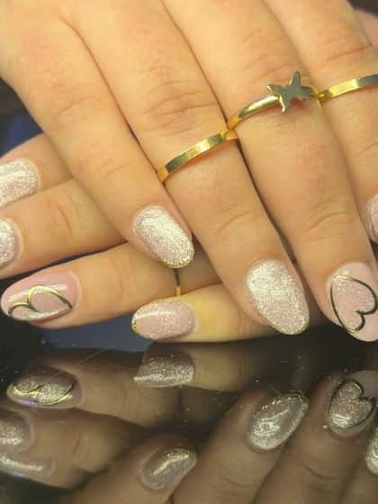 A side view of the glitter and gold heart nail art, styled with gold rings.