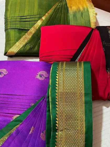 A collection of green, red, and purple sarees, all folded and ready.