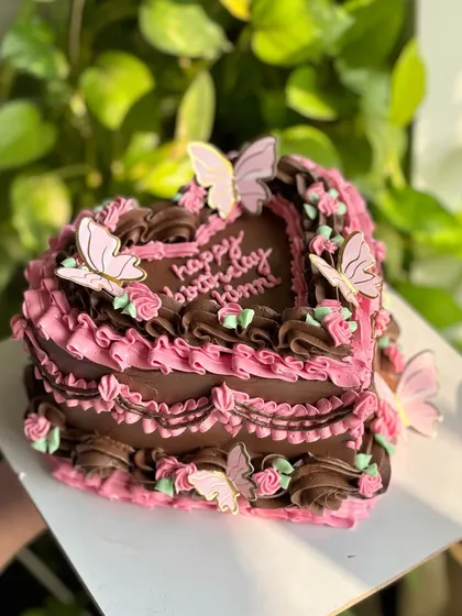 A rich chocolate heart-shaped cake with elaborate pink vintage piping. This design is elevated with whimsical butterfly toppers, creating a dark romantic feel.