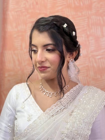 For this bride's church wedding, I created a beautiful braided updo, adorned with small, delicate white flowers. It's an elegant style that perfectly complements her white saree and veil.