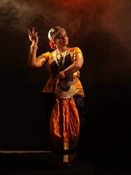A classic Bharatanatyam pose, captured with dramatic lighting and smoke effects to highlight the dancer's form and expression. The full costume is available for rent.