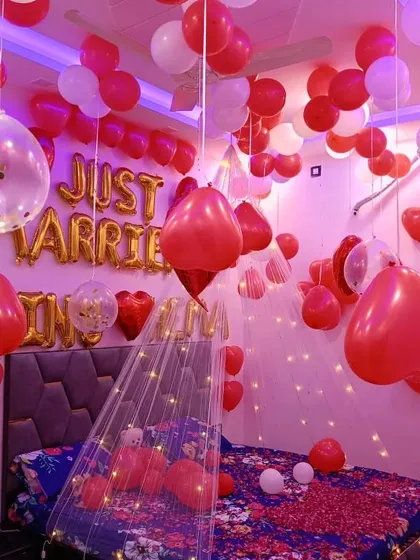 A "Just Married" bedroom decoration. The room is filled with red and white balloons, a light-up canopy, and personalized foil letters on the bed.