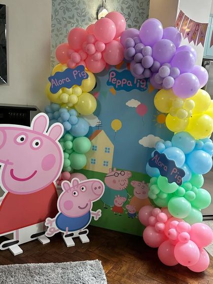 A complete Peppa Pig party scene with a custom printed backdrop showing Peppa's house and family. I framed it with a rainbow of balloons and included large cutouts of Peppa and George for kids to pose with.