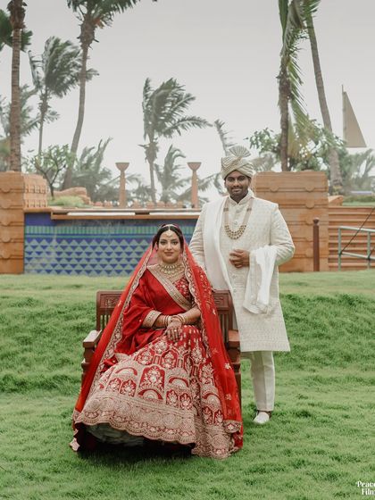 A regal portrait of the couple posing outdoors, the bride seated while the groom stands beside her, set against the backdrop of a luxury resort.