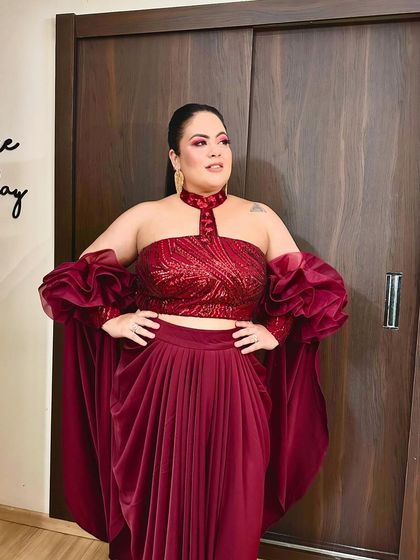 I'm the moonlight. A client looking powerful and glamorous in a custom maroon draped skirt and a sequined, off-shoulder top with dramatic ruffled sleeves.