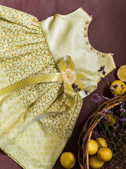 A charming lemon-yellow dress made with multiple fabrics. It combines a solid satin bodice with a floral print and an embroidered overlay skirt for a richly textured look.