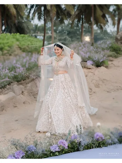 A bride in her own secret garden. I styled this shot on the beach, using lavender flowers to create a dreamy, pastel path. Her white lehenga and flowing veil make her look like an ethereal vision against the coastal landscape.