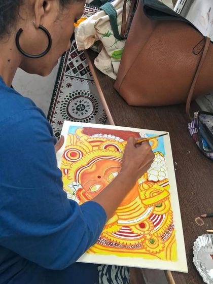 The process of creating a Kerala mural involves careful layering of colors. Here, a student is meticulously filling in the base colors before adding the finer details and outlines.
