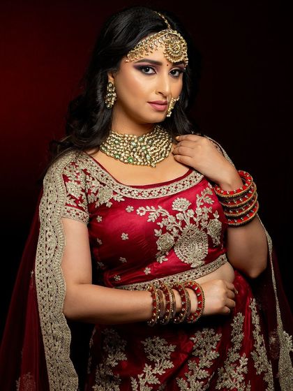 A classic red lehenga look for a North Indian bride. The makeup is kept timeless with gold tones on the eyes and a warm red lip, complemented by a traditional maang tikka and nath.