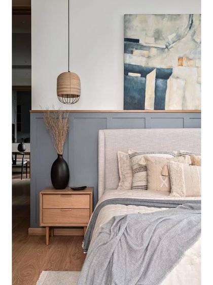 The master bedroom embraces simplicity with a curated color palette. MDF wainscoting painted in a tranquil grey graces half of the bed wall, while the other half remains pristine white, adorned with a captivating abstract artwork.