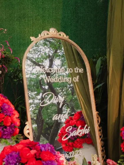 A personalized welcome mirror for the wedding of Divy and Sakshi, surrounded by lush red and purple flowers. A beautiful first impression for the guests.