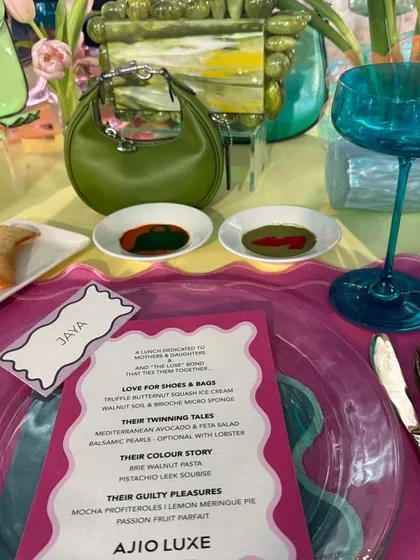 A close-up of a place setting from a couture brunch, showing a personalized menu and artfully smeared sauces that mimic a painter's palette. Every detail is designed to align with the event's creative and high-fashion theme.