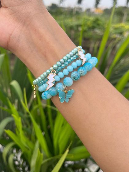 A close-up of a beautiful blue-themed bracelet stack. This set features multiple beaded bracelets with butterfly and lightning bolt charms, perfect for adding a pop of color.