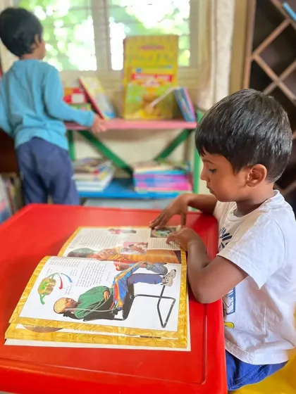 A young boy sits at a child sized table, carefully studying the illustrations in a large book. Our space is equipped with furniture that is perfect for little learners.