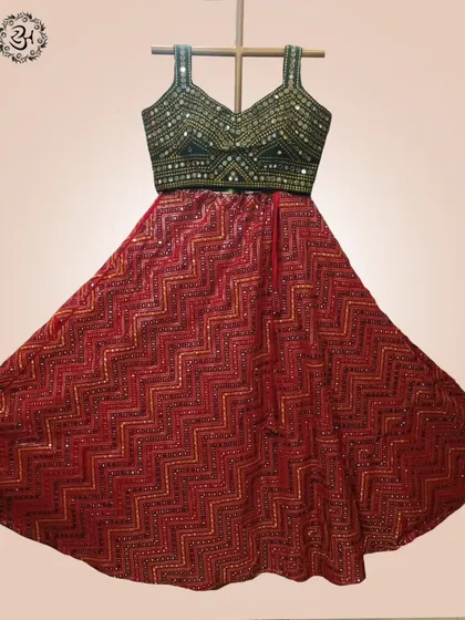 The full flare of the red chevron-patterned lehenga skirt is displayed here. The intricate mirror work on the green blouse adds a touch of sparkle, ideal for festive nights.