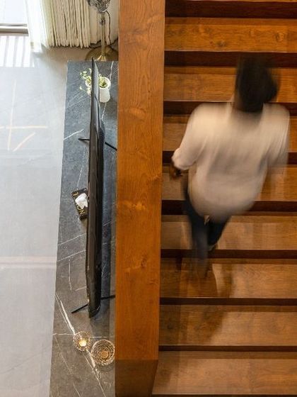 A view from the top of the stairs captures the dynamic movement and verticality within the home. The wooden steps and glass railing maintain a sense of openness, connecting the different levels of the residence.