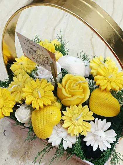 A close-up of the yellow and white candle bouquet in a golden-handled basket.
