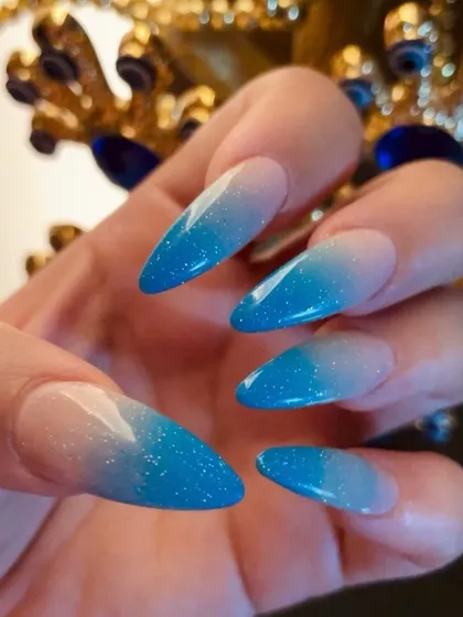 Blue glitter ombré on sharp stiletto nails. The gradient effect from a natural base to a sparkling blue tip is both striking and elegant.