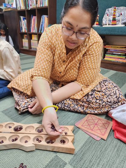 A participant learns to play Pallanguzhi (or Aliguli Mane), a traditional mancala game. This ancient game is excellent for developing math skills, concentration, and strategic thinking.