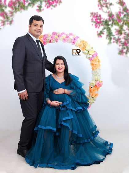 A formal and elegant couple's portrait. The mom-to-be wears a beautiful blue gown, complemented by her partner in a suit, creating a timeless and sophisticated look.