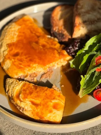 The Braised Lamb Omelette, cut open to show its rich filling, served with a side of fresh salad and toasted sourdough.