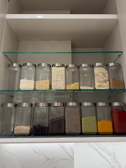This cabinet shelf holds flours, grains like poha, and essential spices. The clear jars and consistent labeling create a cohesive system that simplifies the search for any ingredient.