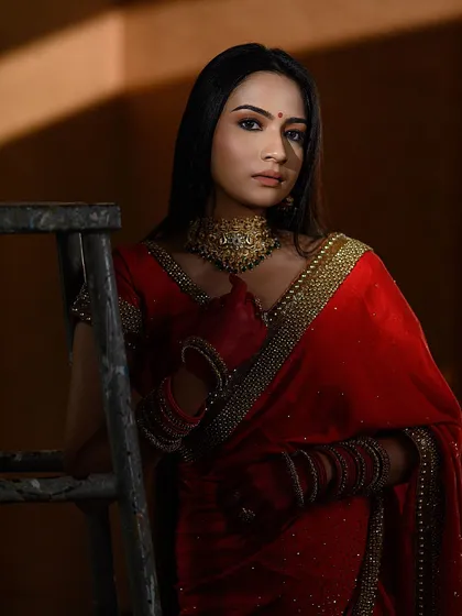 A dramatic portrait using strong shadows from a prop ladder. This adds an unconventional, rustic element to an otherwise traditional red saree look, showing our creative range.
