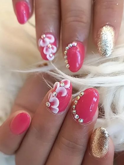 A bright and cheerful set featuring pink nails with 3D flowers, rhinestone cuticle accents, and gold glitter accent nails.