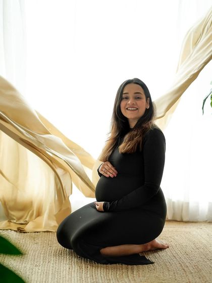 A simple and elegant kneeling portrait in a classic black dress, with a soft fabric creating movement in the background.