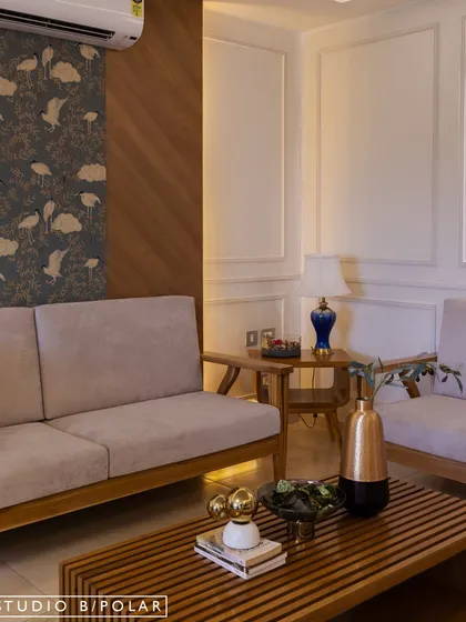 In this Jaipur residence, we used a neutral base and layered it with bold, expressive wallpapers to bring a youthful spark. This living area features a mix of wood paneling, classic molding, and a vibrant bird-patterned wallpaper.