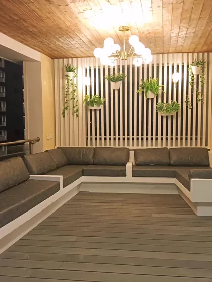 The seating area of the Rajkot balcony project. A custom U-shaped sofa provides ample seating, complemented by a slatted feature wall and a modern chandelier.