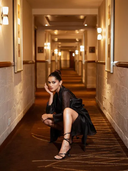 A low-angle shot that uses the corridor's leading lines to create a sense of depth. The crouching pose is edgy and modern, perfect for a high-fashion context.