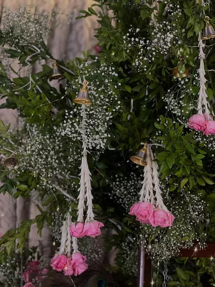 A detailed shot of the hanging floral decorations. Delicate tassels made of white jasmine and pink roses, accented with tiny bells, hang from the green canopy, adding movement and charm.
