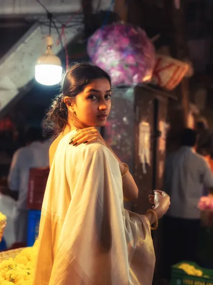 In the middle of a bustling Mumbai flower market, the single light source illuminates the model, creating a soft, painterly effect.