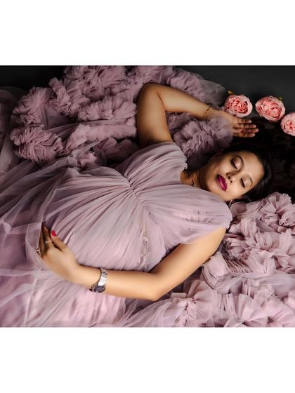 An artistic overhead shot of an expectant mother lying down, her lavender gown spread out around her with a crown of pink roses in her hair. This composition is both romantic and visually striking.
