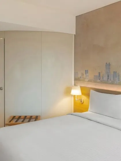 Another view of the IBIS Thane guest room, highlighting the efficient layout, including the curved wall of the bathroom pod and the open luggage rack, all designed for the modern traveler.