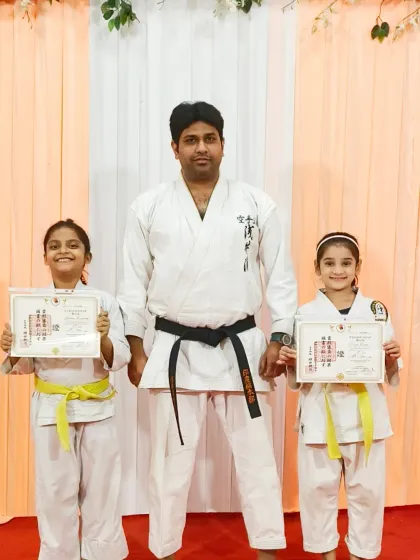 Two young warriors proudly holding their yellow belt certificates at the Rejoice International School event.