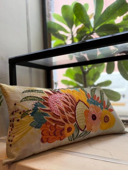 This lumbar cushion features a stunning, hand-embroidered bouquet of protea flowers. The vibrant colors and intricate beadwork make it a true statement piece, showcasing our commitment to wearable art.